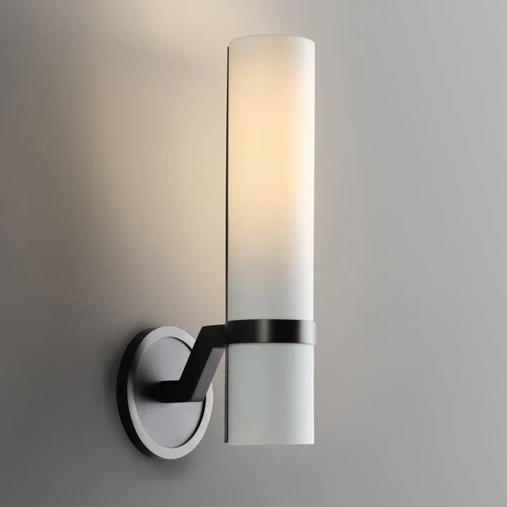 Wall-mounted light fixture with cylindrical glass shade on a gray background